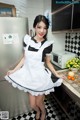 A woman in a maid outfit posing in a kitchen.