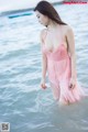 A woman in a pink dress standing in the water.