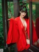 A woman in a red robe is posing by a window.