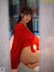 A woman in a red robe sitting on a bed.