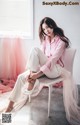 A woman sitting on a chair in a pink shirt and white pants.