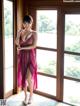 A woman in a pink dress standing by a window.