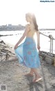 A woman in a yellow top and blue skirt walking on the beach.