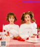 two girls sitting at a table with strawberries on it