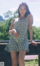 A woman in a floral dress leaning against a wall.