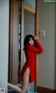 A woman in a red dress leaning against a door.