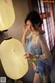 A woman in a kimono standing next to a lamp.