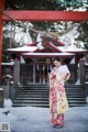 A woman in a kimono standing in front of a red gate.