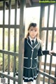 A woman in a school uniform leaning against a fence.