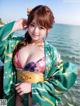 A woman in a green kimono posing by the water.