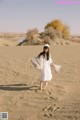 A woman in a white dress is walking in the sand.