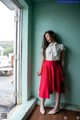 A woman in a white shirt and red skirt leaning against a window.