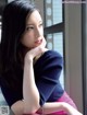 A woman sitting on a window sill with her hand on her chin.