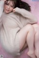 A woman in a beige sweater is sitting on a pink blanket.