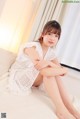 A woman in a white dress sitting on a bed.