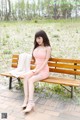 A woman in a pink dress sitting on a wooden bench.