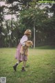 A little girl walking in a field holding a teddy bear.