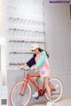 A woman riding a red bike in front of a wall of glasses.