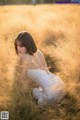 A woman in a white dress crouching in a field of tall grass.