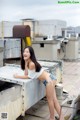 A woman in a white top and blue shorts posing on a rooftop.