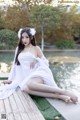 A woman in a white dress sitting on a wooden dock.