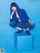 A woman with blue hair sitting on a blue cube.